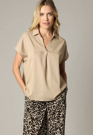 Blouse beige à manches courtes avec un col, présentant un décolleté en V. Assortie avec un pantalon ample à imprimé léopard. Tissu doux, coupe décontractée.