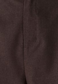 Donkerbruin stofdetail van een textiel met een gestructureerd oppervlak, met een zichtbare naad en een ontwerp voor een zijzak.