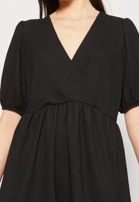 Vestido negro con escote cruzado, mangas abullonadas cortas y cintura fruncida. La tela presenta un acabado texturizado.