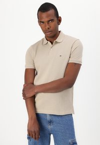 Bežové polo tričko s texturovanou tkaninou, krátkými rukávy a slim fit střihem. Obsahuje malé značkové logo na hrudi. Casual design.