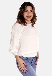 Maglione bianco con scollo ampio e maniche lunghe, abbinato a jeans azzurri chiari, caratterizzato da una texture morbida e una vestibilità comoda.