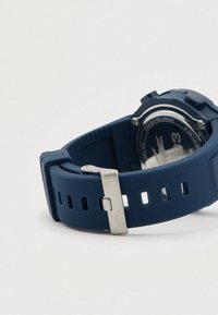 Bracelet de montre bleu texturé avec boucle en argent posé à plat, dos de montre en acier inoxydable visible avec inscription et design gravés.