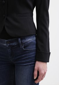 Svart skräddarsydd blazer med smal passform, en knappstängning och en slät yta, kombinerad med mörkblå jeans med en klassisk femficksdesign.
