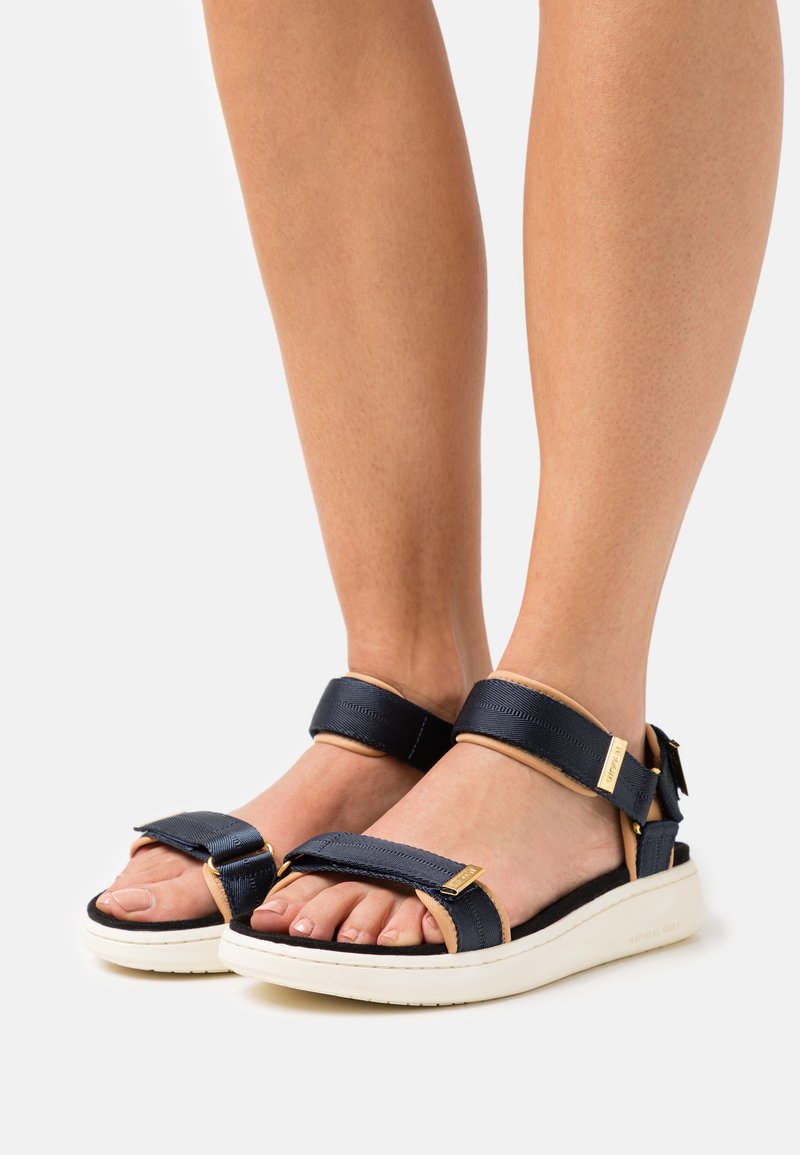 Sandalias azul marino con correas de tela ajustables, acentos beige, suela acolchada y detalles en hardware dorado. Diseño destalonado.