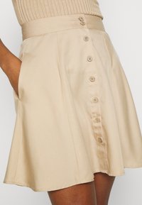 Högmidjad beige kjol med knäppning fram och sidofickor, bärs med en beige ribbad topp.