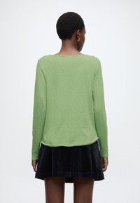 Zielona bluzka z długim rękawem o okrągłym dekolcie i luźnym kroju, zestawiona z czarną spódnicą ze sztruksu z rozkloszowanym dołem.