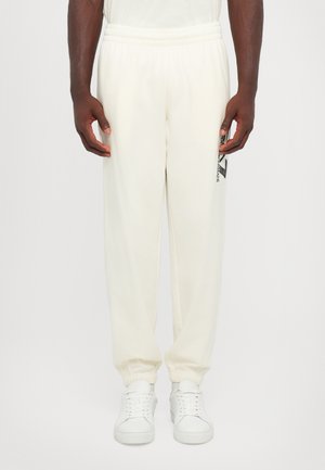 Cream-colored sweatpants with an elastic waist, cuffed ankles, and a side logo print. Smooth fabric texture, relaxed fit.