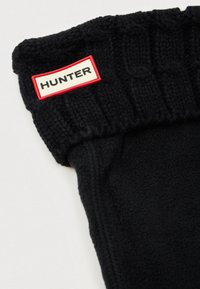 Melnas flokšādas zābaku oderes ar ribotu adījumu pie kakla. Augšpusē iekļauts sarkans un balts "HUNTER" etiķete. Mīksta tekstūra un cieši pieguļoša forma.