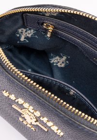 Pungă din piele texturată navy cu fermoar și elemente de metal aurii. Interiorul are o căptușeală din material închis la culoare cu un model discret de logo.