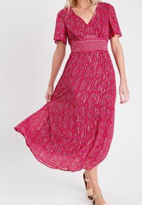 Robe maxi fuchsia avec imprimé floral, dotée de manches courtes, d'une taille smockée et d'une jupe fluide en tissu léger.