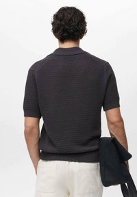 Polo shirt a maniche corte di colore grigio scuro, lavorato a maglia, con colletto e orlo a coste, caratterizzato da un motivo testurizzato. Indossato con pantaloni chiari.