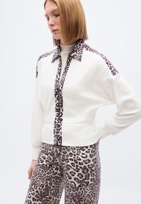 Λευκό τοπ με γιακά και εμπρόσθιο πάνελ με λεοπάρ σχέδιο· σετ με παντελόνι με το ίδιο λεοπάρ σχέδιο· μαλακό ύφασμα· άνετη εφαρμογή.