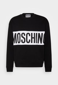 Felpa nera con una banda orizzontale bianca che presenta il testo "MOSCHINO". Collo rotondo, maniche lunghe, polsini e orlo a costine. Tessuto morbido.