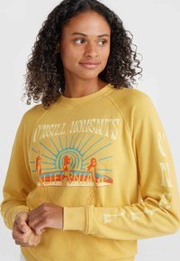 Felpa gialla con una vestibilità morbida, caratterizzata da un design grafico di surfisti e testo "CALIFORNIA". Maniche lunghe con dettagli stampati.