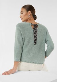 Hellgrüner gestrickter Pullover mit Dreiviertelärmeln, der ein Keyhole-Rückenteil und ein Leopardenmuster-Knoten-Detail aufweist. Weicher Stoff und lockere Passform.