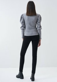 Maglione grigio lavorato a maglia con maniche a sbuffo, silhouette aderente e dettagli con bottoni sui polsini, abbinato a pantaloni neri slim-fit e stivaletti.