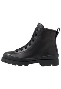 Bottine en cuir noir avec bout rond, devant à lacets, tige texturée et semelle en caoutchouc chunky. Dispose d'une languette à l'arrière.