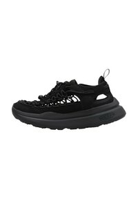 Zapatilla negra con un upper de malla y ante, que presenta una suela de goma gruesa, un detalle tejido en la parte delantera y cortes en los lados.