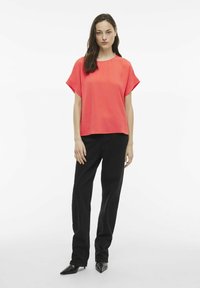Top corto corallo con un tessuto texturizzato, abbinato a pantaloni neri a vita alta e scarpe nere appuntite, con una vestibilità rilassata.