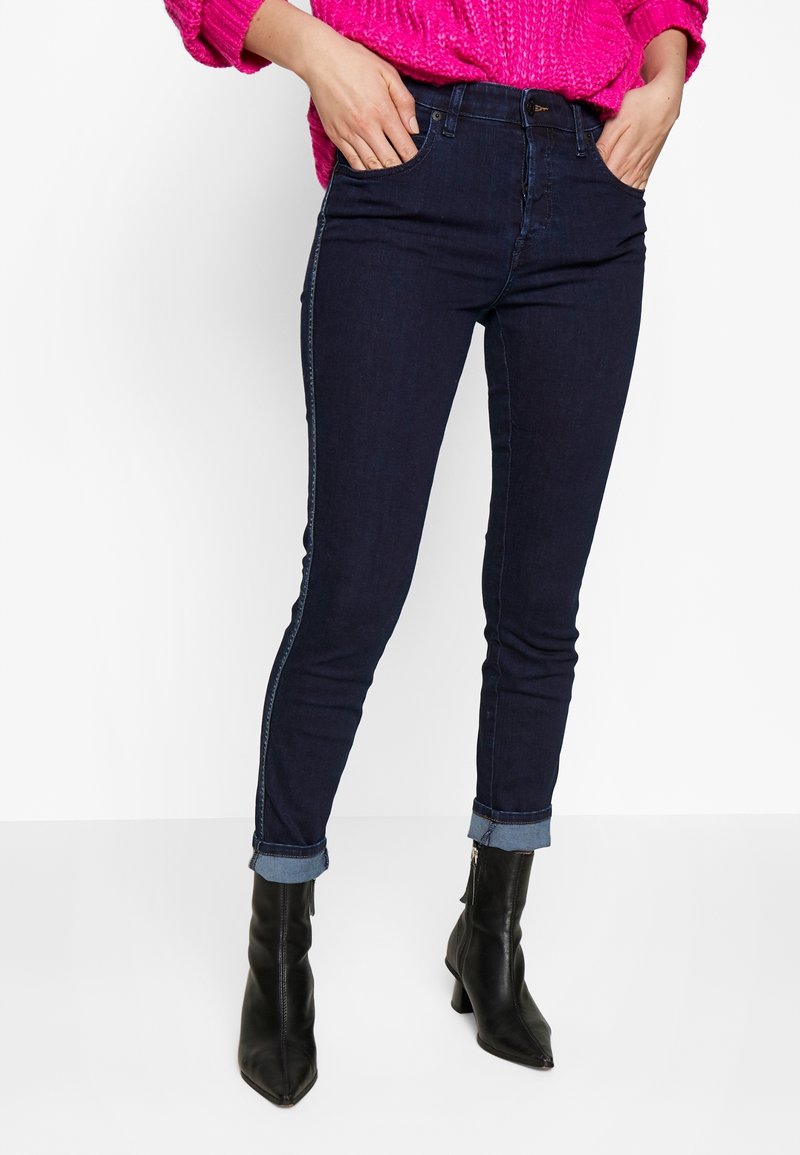 Mörkblå denimjeans med slim fit, med uppvikta ben och kontrasterande sidostygn, matchade med svarta ankelboots.