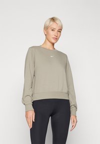 Felpa grigio chiaro con scollo rotondo e maniche lunghe, con logo Nike bianco sul petto. Abbinata a leggings neri.