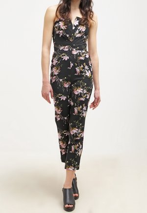 Zwarte bloemen jumpsuit met een strakke strapless lijfje, voorzien van een ruches-neklijn en roze en groene bloemenpatronen.