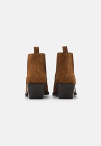 Bottines en daim marron avec un talon empilé, dotées de coutures simples et d'une languette à l'arrière pour un enfilage facile.