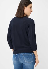 Pullover leggero blu navy con maniche a tre quarti, orlo a coste e vestibilità rilassata. Indossato con jeans azzurri leggeri con tasche posteriori.