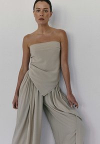 Beżowy top bez ramiączek z drapowanym przodem, w połączeniu z luźnymi, szerokimi spodniami o plisowanych detalach w tym samym kolorze.