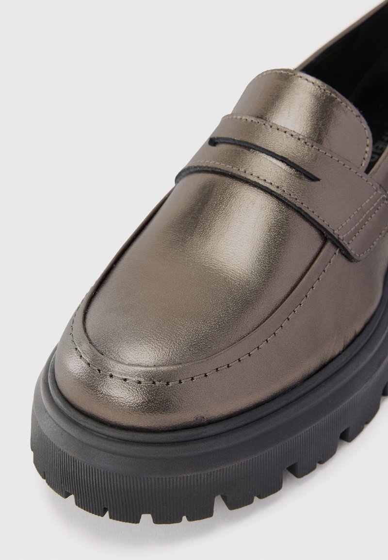 Metaliczne szare loafersy o gładkim wykończeniu, z wyraźnym paskiem i grubą czarną gumową podeszwą z teksturowanym bieżnikiem.
