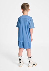Tenue de sport bleue composée d'un t-shirt à manches courtes et d'un short, en tissu lisse, accompagnée de chaussettes blanches ornées de motifs en chevron noirs.