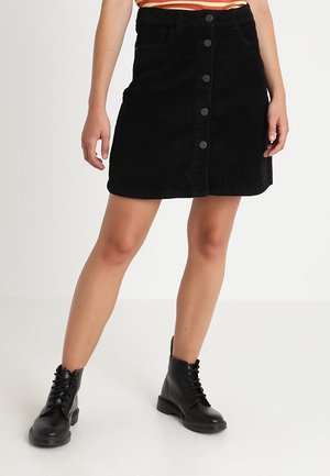 Czarna spódnica sztruksowa z zapięciem na guziki z przodu, z dwoma bocznymi kieszeniami i prostą sylwetką. Noszona z czarnymi botkami sznurowanymi.