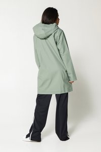 Long, waterproof green coat with hood, features a straight cut and loose fit. Paired with black pants and white sneakers.