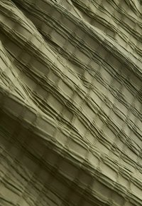 Texturiertes olivgrünes Gewebe mit einer geriffelten Oberfläche, das ein Karomuster aufweist, das durch erhöhte Nähte und eine glatte Fläche entsteht.