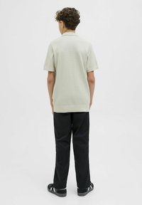 Ljusgrå kortärmad polo med strukturerad tyg, ihop med svarta byxor och sandaler, sedd från baksidan.