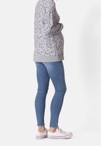 Pull décontracté de couleur violet clair avec un motif floral, des bordures grises et des accents de boutons. Porté avec un jean skinny bleu et des baskets blanches.
