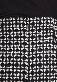 Svart och vit texturerad tyg med ett rutmönster, med en mjuk, vävd utseende och synliga tråddetaljer.