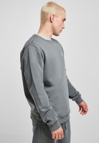 Felpa grigia in tessuto morbido, con scollo tondo, polsini a costine e un piccolo logo sul petto, abbinata a pantaloni della tuta coordinati.