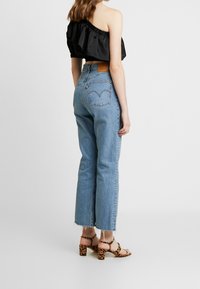 Ljusblå högmidjade jeans med raka ben, fransad nederkant och läderlagg i bakfickan. Kombinerat med en svart off-the-shoulder topp och klackar med leopardmönster.