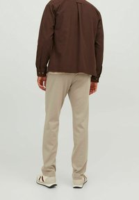 Brązowa koszula na guziki z plisą z tyłu, zestawiona z jasnobeżowymi spodniami. Białe buty z czerwonymi paskami po bokach.