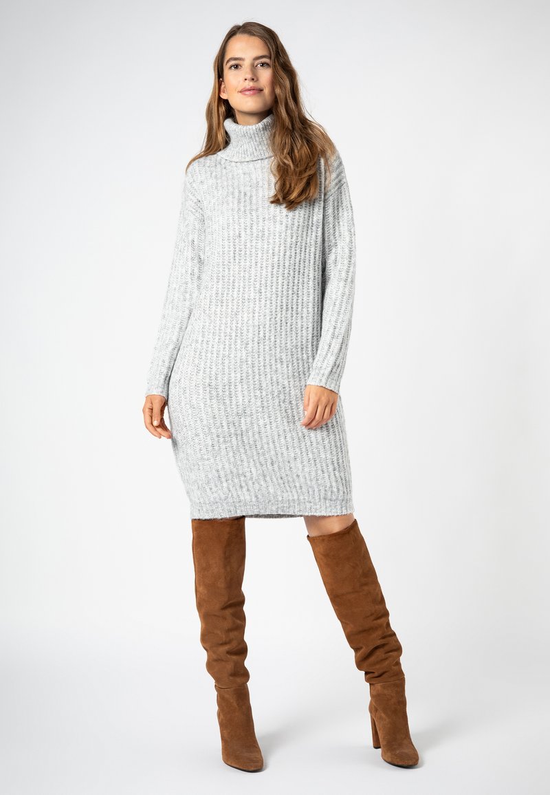 Graues geripptes Rollkragenkleid, knielang, aus Strickmaterial; kombiniert mit braunen Wildleder-Stiefeln über das Knie; Model steht.