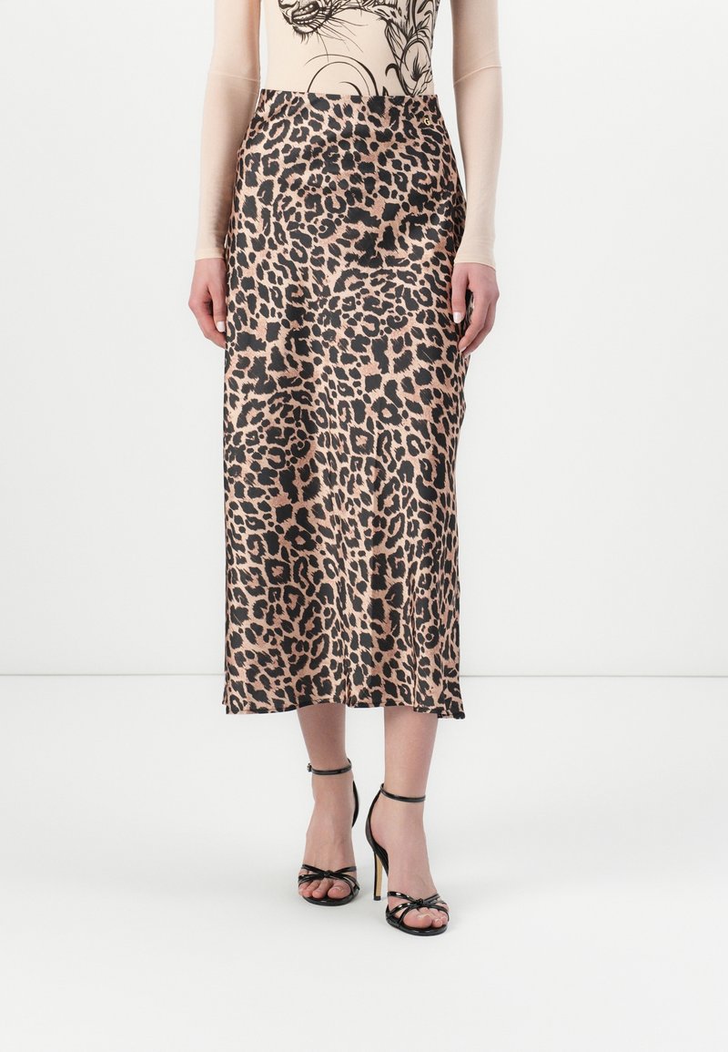 Femme portant une jupe midi imprimé léopard associée à des sandales noires à talons hauts et à brides, et un haut beige avec un imprimé tigre.
