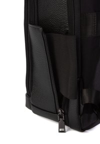 Lähikuva mustast nahast ja kangast kotist, mille nurgas on osaliselt avatud tõmblukk, paljastades sisemuses elastse rihma.