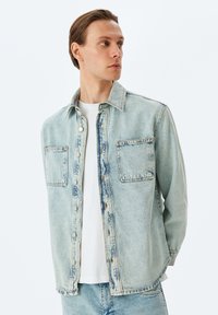 Vaaleansininen farkkupaita, jossa on kaksi rintataskua, napitus ja klassinen kaulus. Kuitenkin valkoisen t-paidan päällä, omaa rentoa istuvuutta.