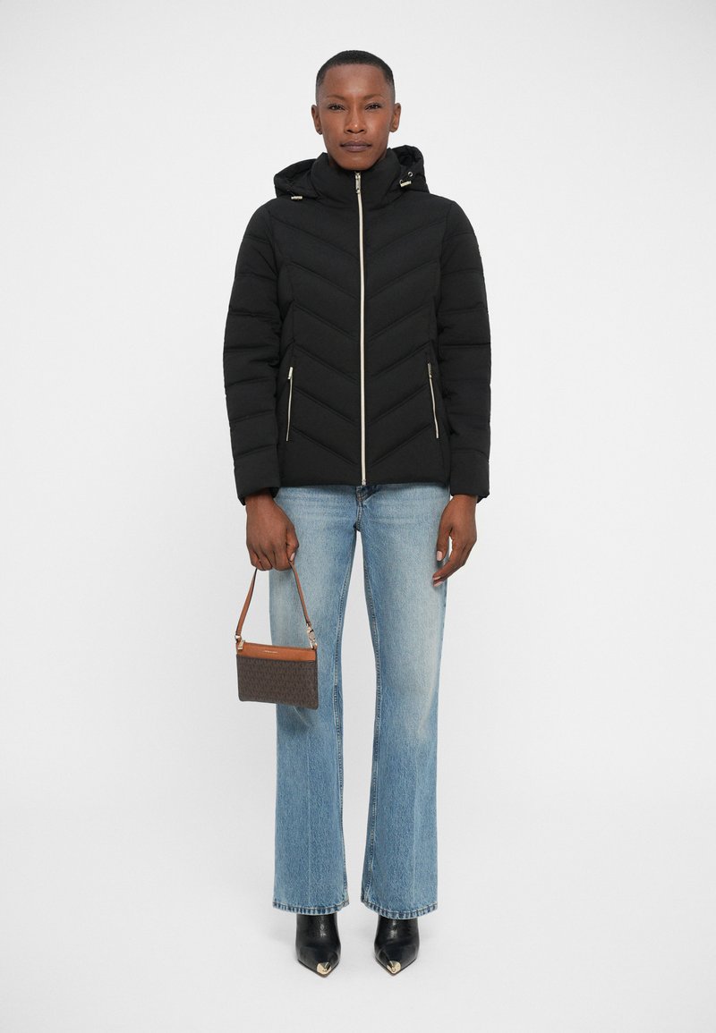 Black puffer jacket with chevron design, hood, gold zipper, paired with light blue flared jeans and a brown handbag with a strap. Black pointed-toe boots.