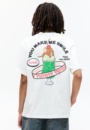 Hvid T-shirt med et grafik, der viser en tegneserie-mus og en grøn dessertkop. Teksten inkluderer "Du gør mig glad" og "Sød lækker lækker" i fed skrift.
