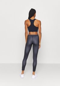 Marinblå sportbh med racerback-design i kombination med mörkgrå leggings som har en blänkande yta och en figurnära silhuett, accentuerad av subtila sömmar.