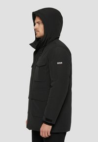 Sort isoleret jakke med hætte, forlommer og et logo på ærmet. Har lynlåslukning og tekstureret stof.