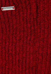 Roter Strickstoff mit gerippter Textur, versehen mit einem silbernen Markenschild, das in das Gewebe eingearbeitet ist, um zusätzliche Details zu bieten.