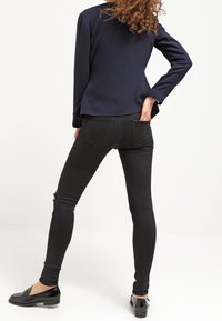 Černé skinny džíny s dírami na kolenou, doplněné námořnickým sako. Model má na sobě černé mokasíny, které zdůrazňují elegantní siluetu.